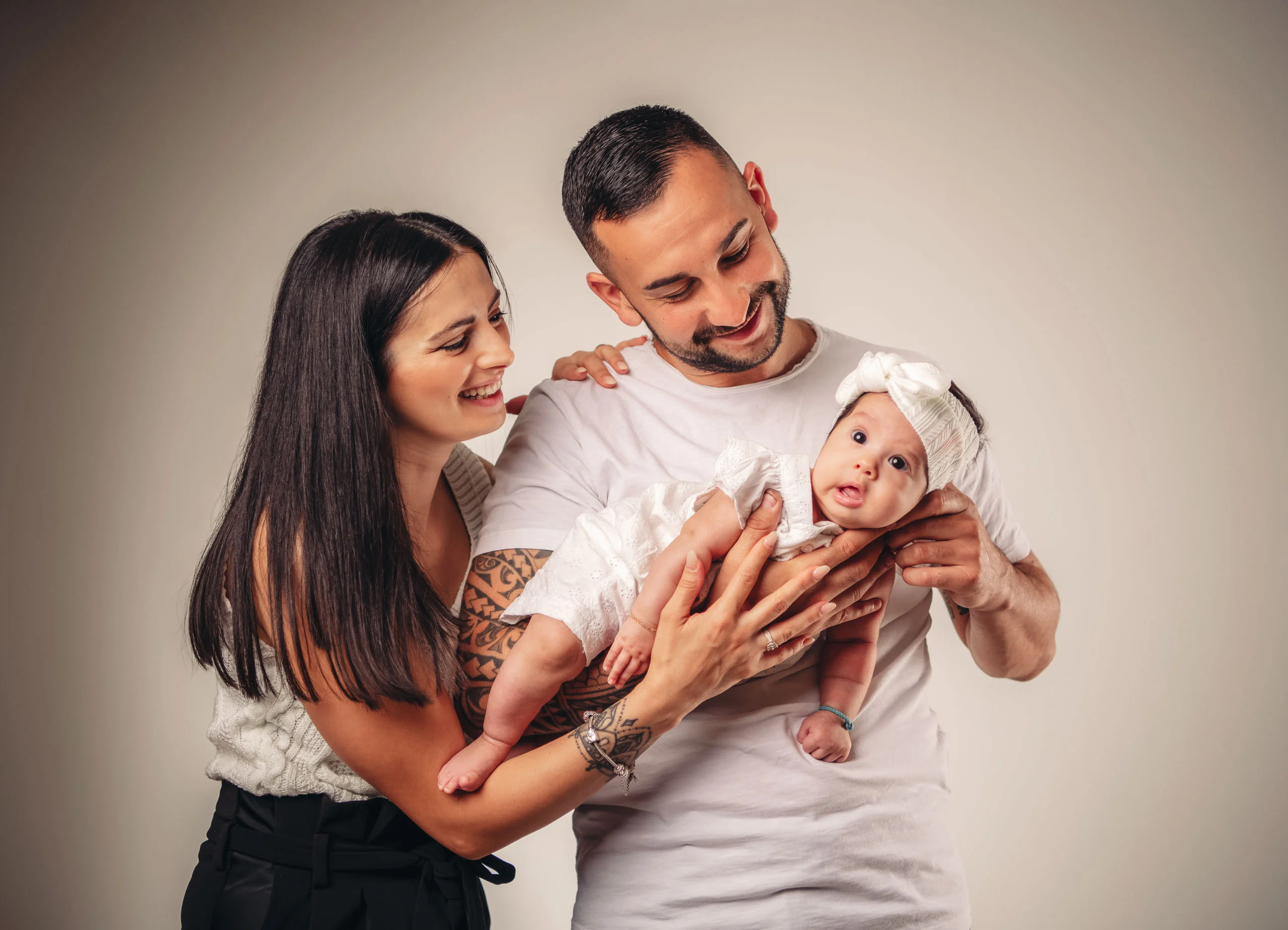 Familienfotos Produktbild 14 | Peter Lauritis Photography Eltern lachen ihr Baby mit weißer Haarschleife an, das der Vater hochhält
