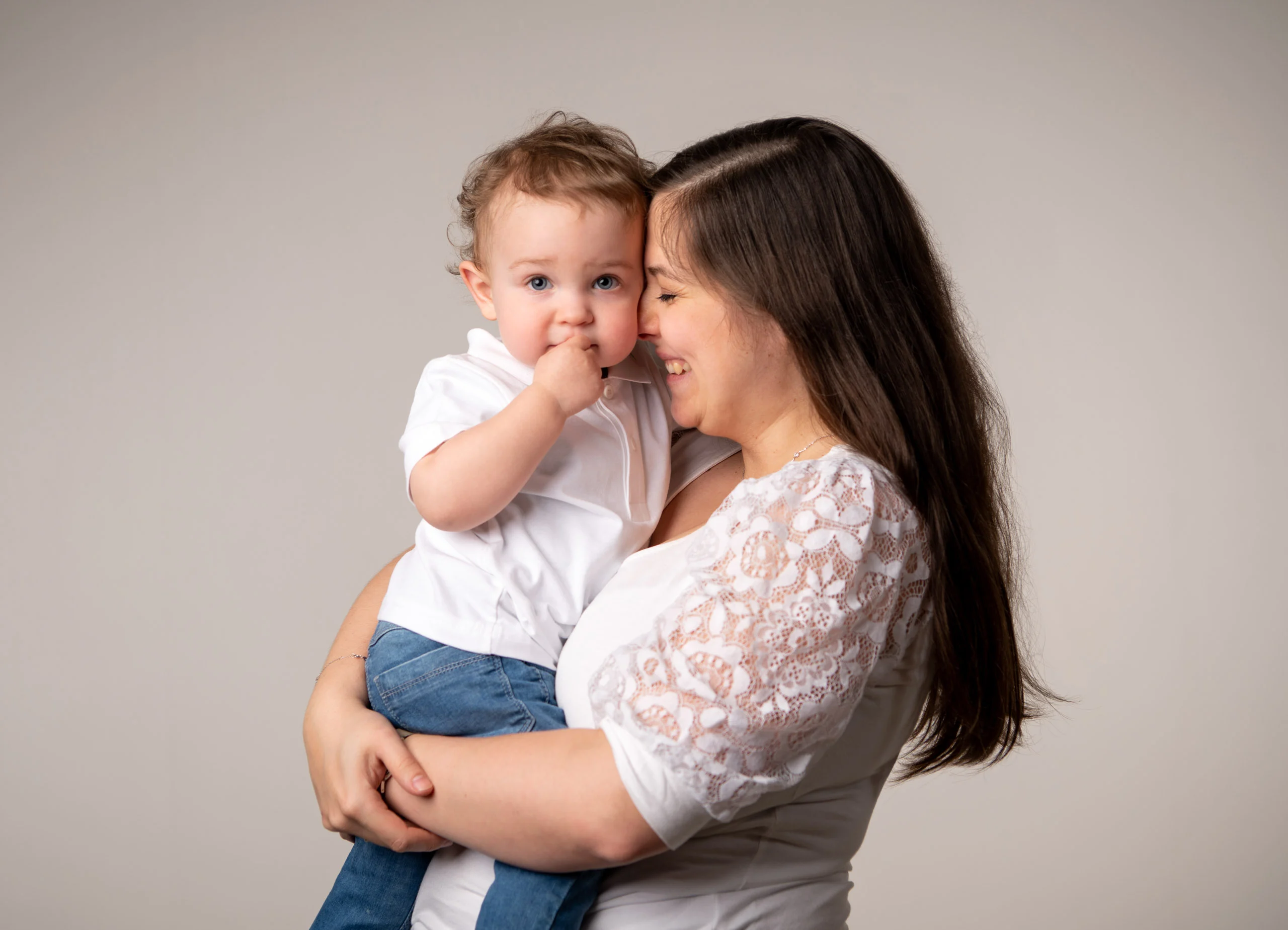 Familienfotos Produktbild 16 | Peter Lauritis Photography Frau mit langen dunklen Haaren hält ein Kleinkind auf dem Arm, das sich die Hand an den Mund hält