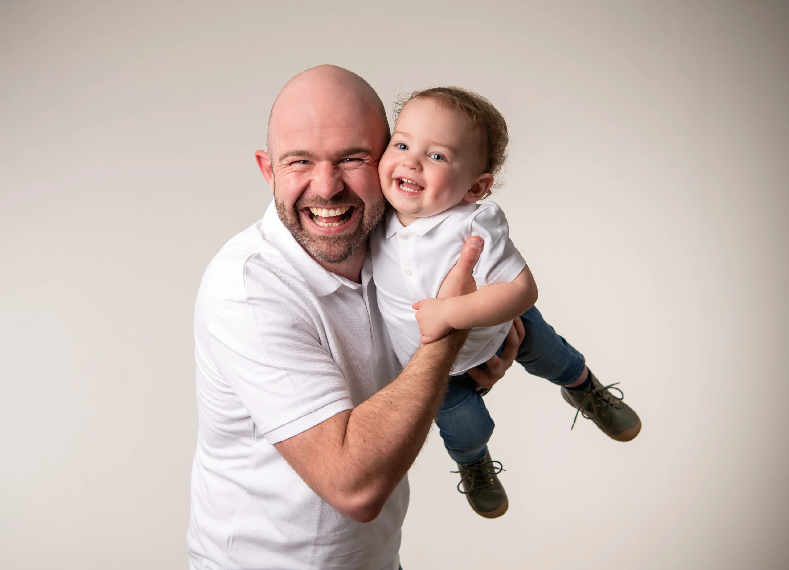Familienfotos Produktbild 17 | Peter Lauritis Photography Lachender Mann hält ein Kleinkind im Arm, beide in Weiß