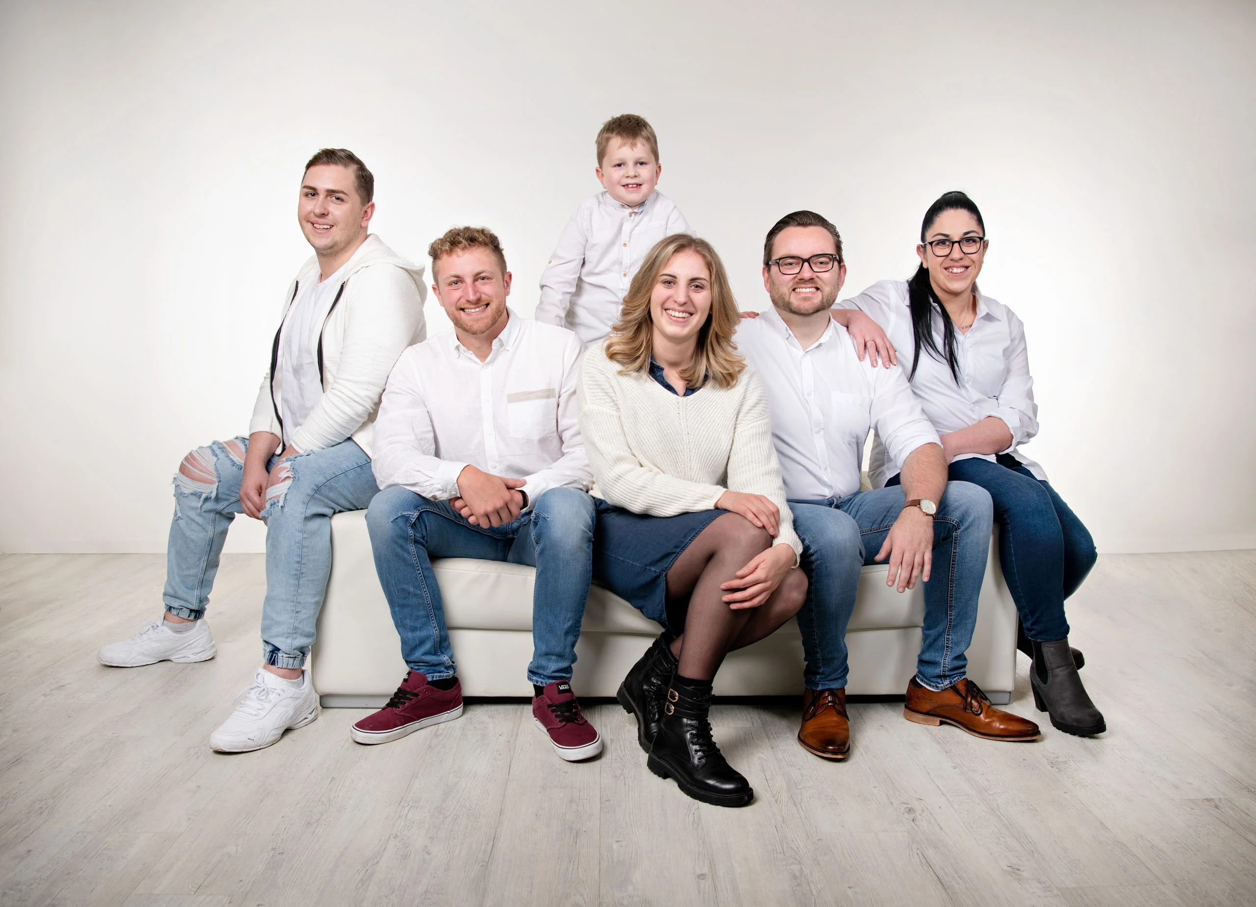 Familienfotos Produktbild 23 | Peter Lauritis Photography Sechs Erwachsene und ein Kind sitzen in Weiß und Jeans auf einem weißen Sofa