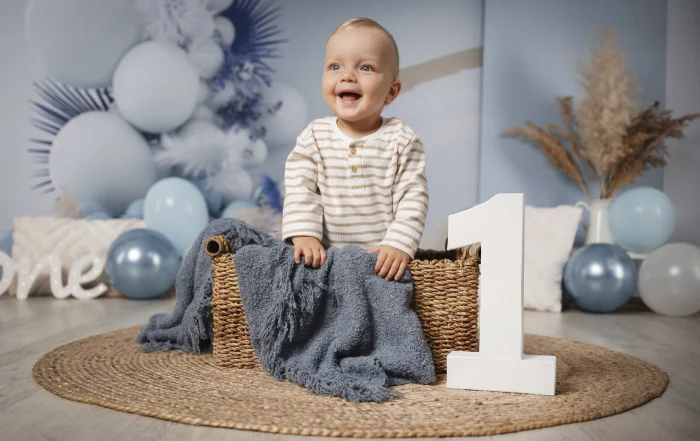 Cake Smash: Junge mit großer weißer Eins vor blauen Luftballons | Peter Lauritis Photography Cake Smash für Jungen: Einjähriger sitzt lachend im Korb mit blauer Decke neben einer großen weißen Eins vor blauen Luftballons