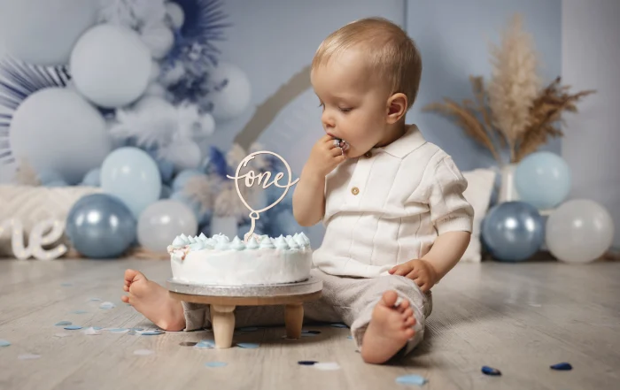 Geburtstagskind probiert die Torte | Peter Lauritis Photography Einjähriger Junge steckt sich beim Cake Smash ein Stück Torte in den Mund, daneben die weiße Torte mit One-Topper