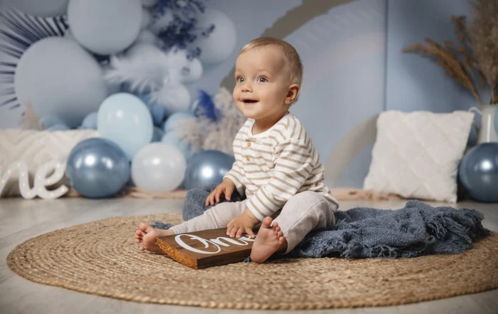 Junge mit One-Schild auf dem Juteteppich | Peter Lauritis Photography Kleiner Junge mit blauen Augen sitzt auf einem Juteteppich mit blauer Decke und hält ein Holzschild mit der Aufschrift One