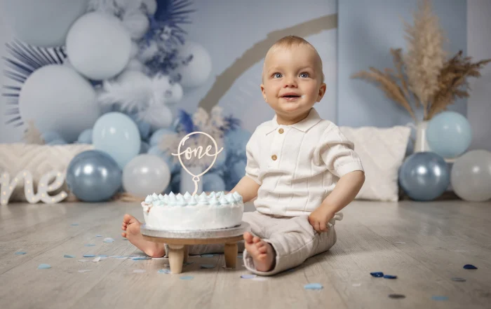 Cake Smash: Junge vor seiner Geburtstagstorte | Peter Lauritis Photography Cake Smash: Junge im weißen Strickshirt sitzt vor einer weißen Torte mit hellblauen Tupfen und One-Topper