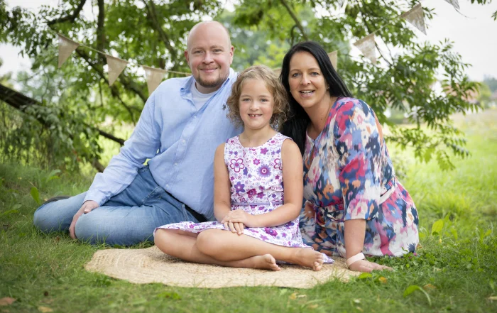 Familienfoto zur Einschulung | Peter Lauritis Photography Eltern sitzen mit ihrer Tochter zur Einschulung auf einer Jutematte auf der Wiese und lächeln in die Kamera