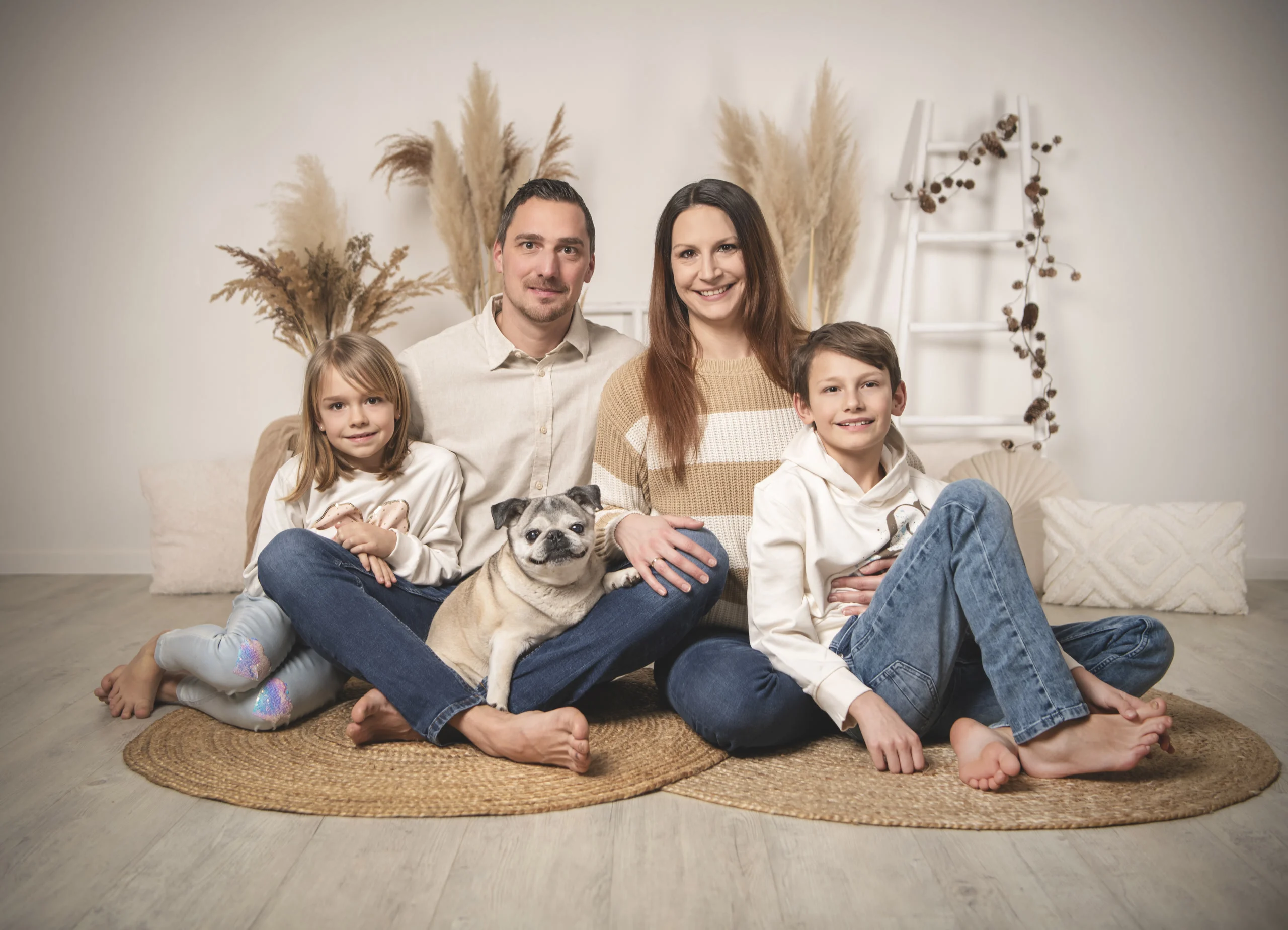 Familienfoto mit Eltern, zwei Kindern und Mops | Peter Lauritis Photography | Peter Lauritis Photography Familienfotos mit Hund: Eltern, Tochter und Sohn sitzen lachend auf Juteteppichen, in der Mitte ihr Mops