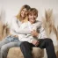 Fotoshooting vor Weihnachten: Teenager-Schwester umarmt ihren Bruder, beide sitzen lachend auf einem Hocker vor Pampasgras