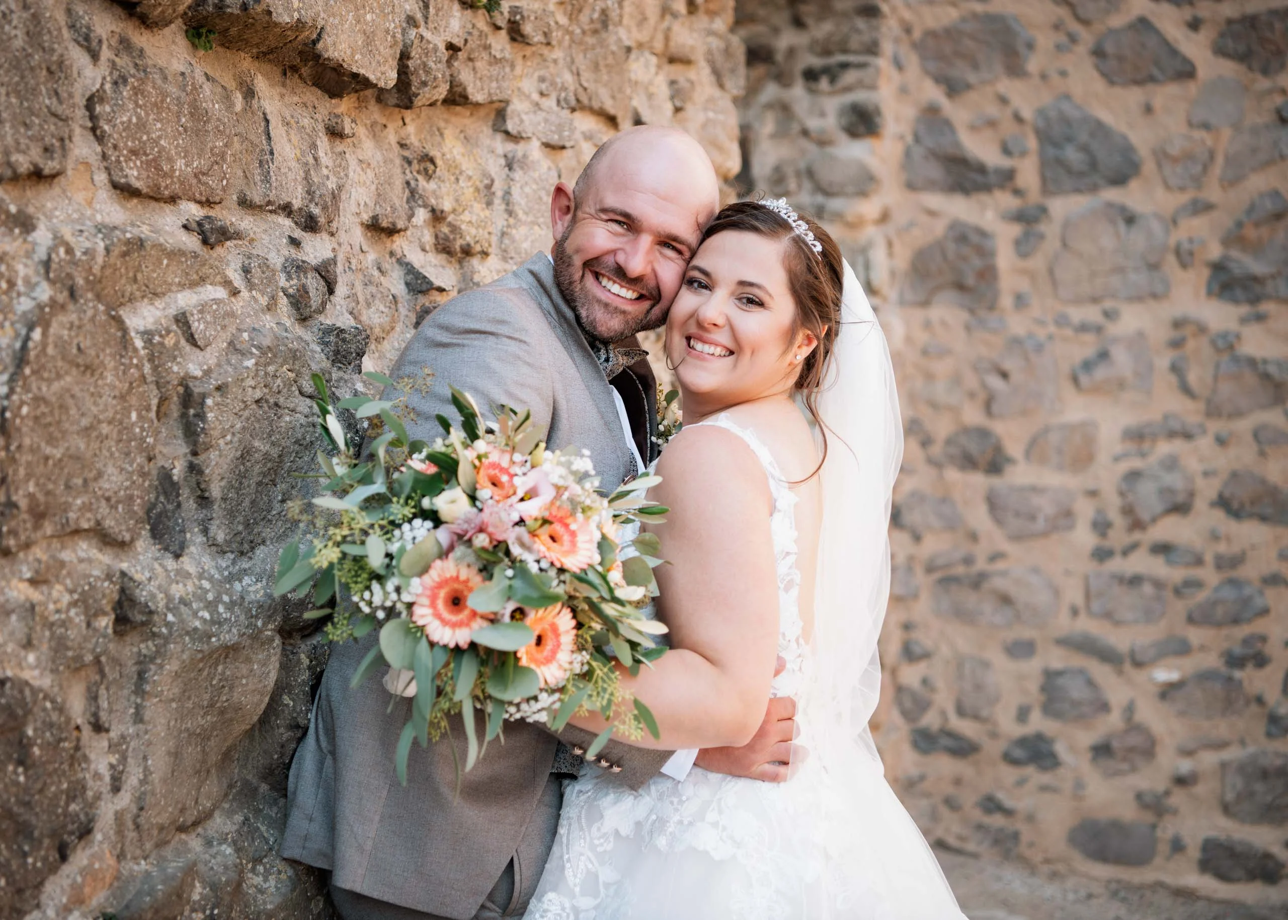 Hochzeitspakete – Brautpaar vor Steinmauer | Peter Lauritis Photography Hochzeitspakete: Brautpaar lacht mit Brautstrauß vor einer Steinmauer