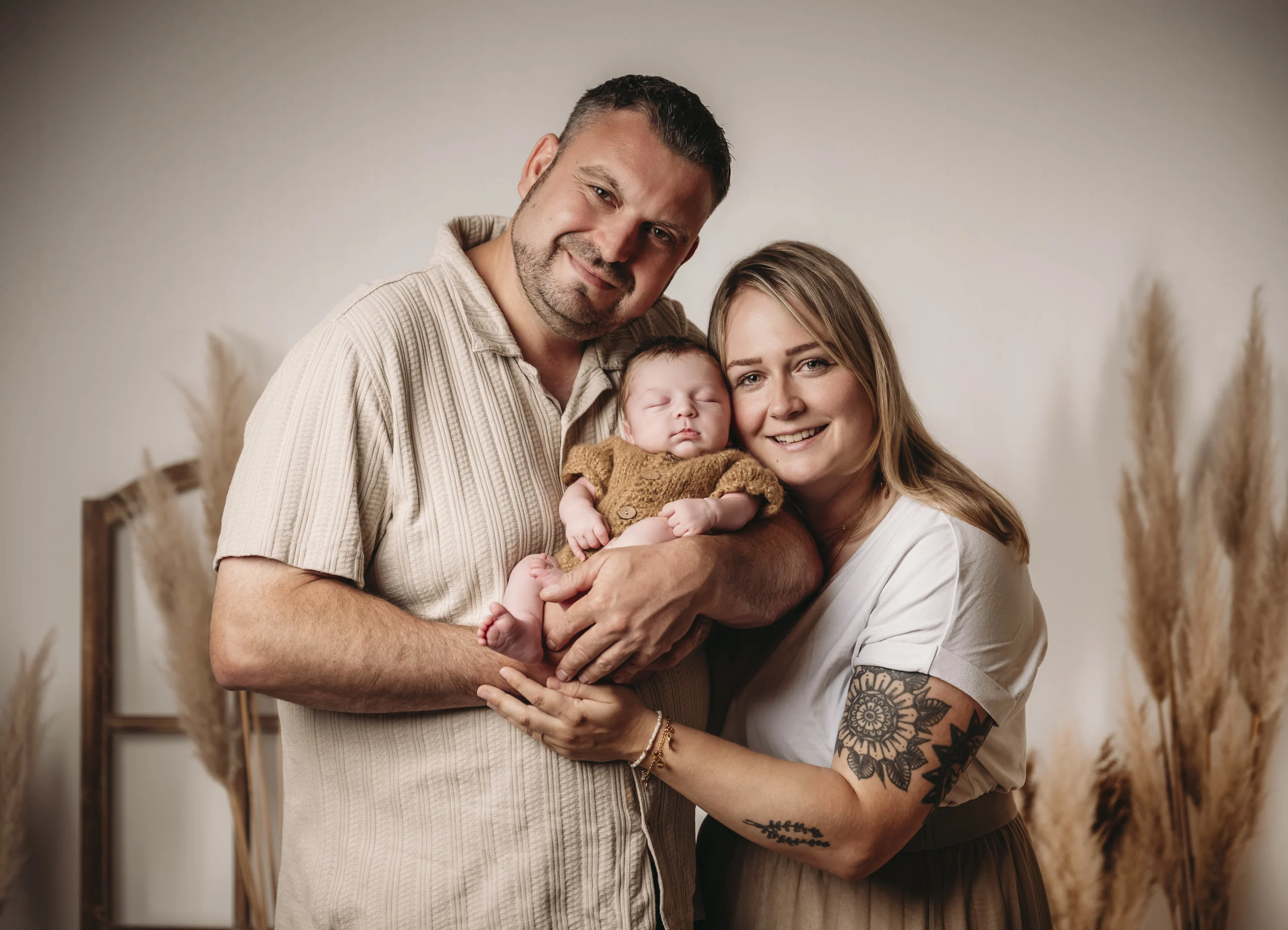 neugeborene eltern laecheln fotostudio | Peter Lauritis Photography Glückliche Eltern halten ihr Neugeborenes im Fotostudio vor Pampasgras – Neugeborenen-Fotoshooting in Neustadt (Hessen)