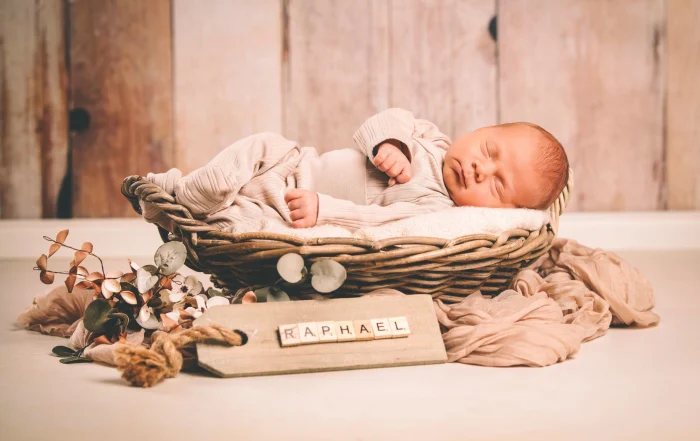 Neugeborenes schläft im Weidenkorb mit Namensschild | Peter Lauritis Photography Neugeborenes Baby schläft im Weidenkorb, davor ein Holzschild mit seinem Namen
