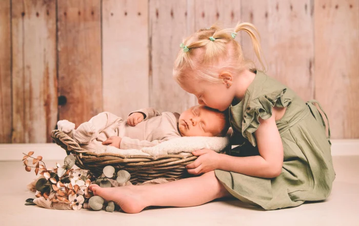 Große Schwester küsst ihren neugeborenen Bruder auf den Kopf | Peter Lauritis Photography Große Schwester küsst ihren schlafenden neugeborenen Bruder im Korb auf den Kopf