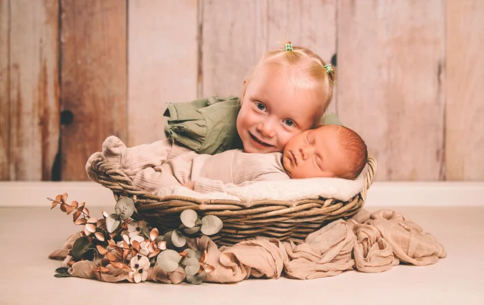 Stolze große Schwester kuschelt Wange an Wange mit dem Neugeborenen | Peter Lauritis Photography Große Schwester kuschelt Wange an Wange mit ihrem schlafenden Baby-Bruder im Weidenkorb
