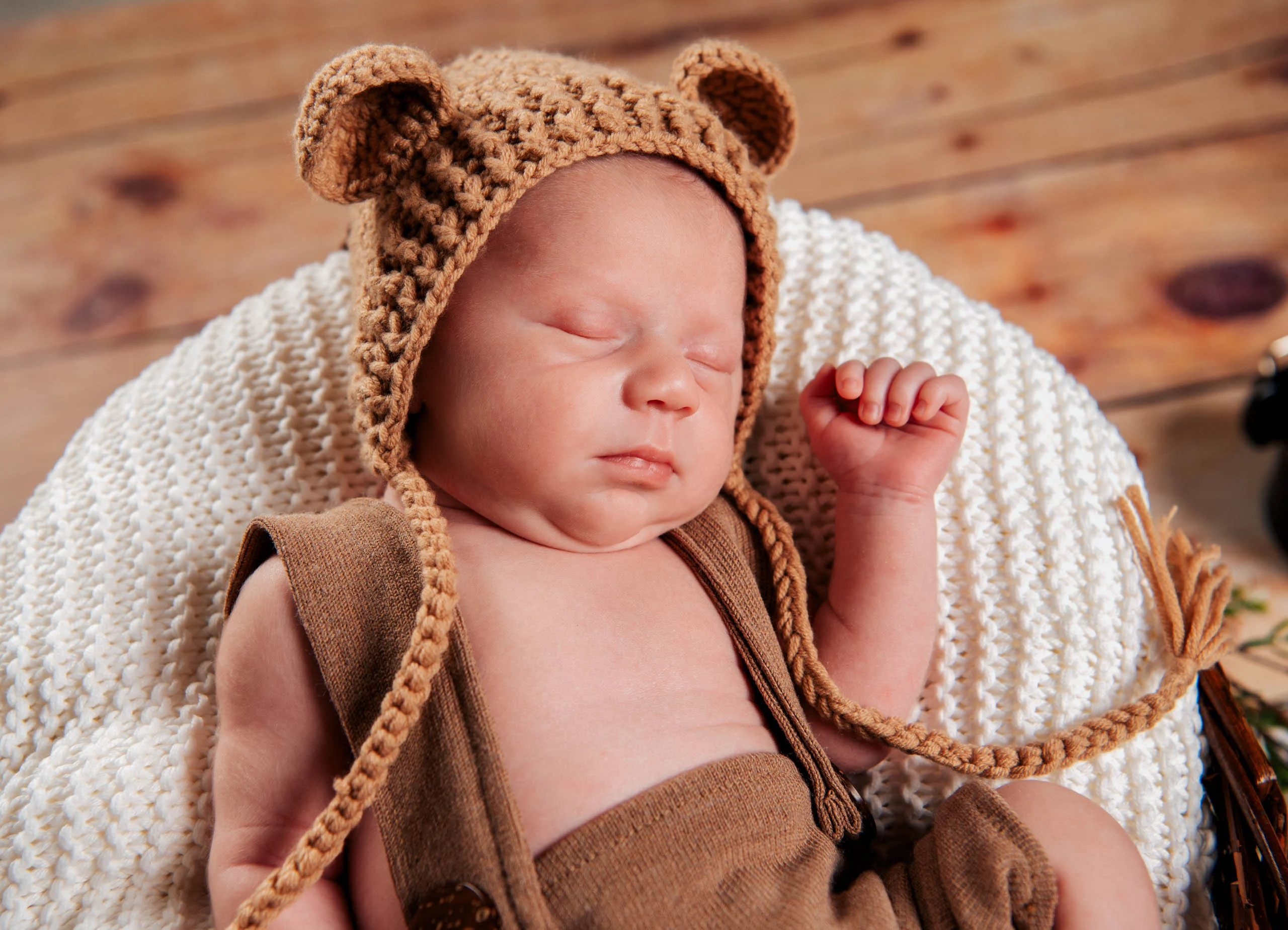 Babypass: schlafendes Neugeborenes mit gehäkelter Bärenmütze und brauner Latzhose auf einer weißen Strickdecke