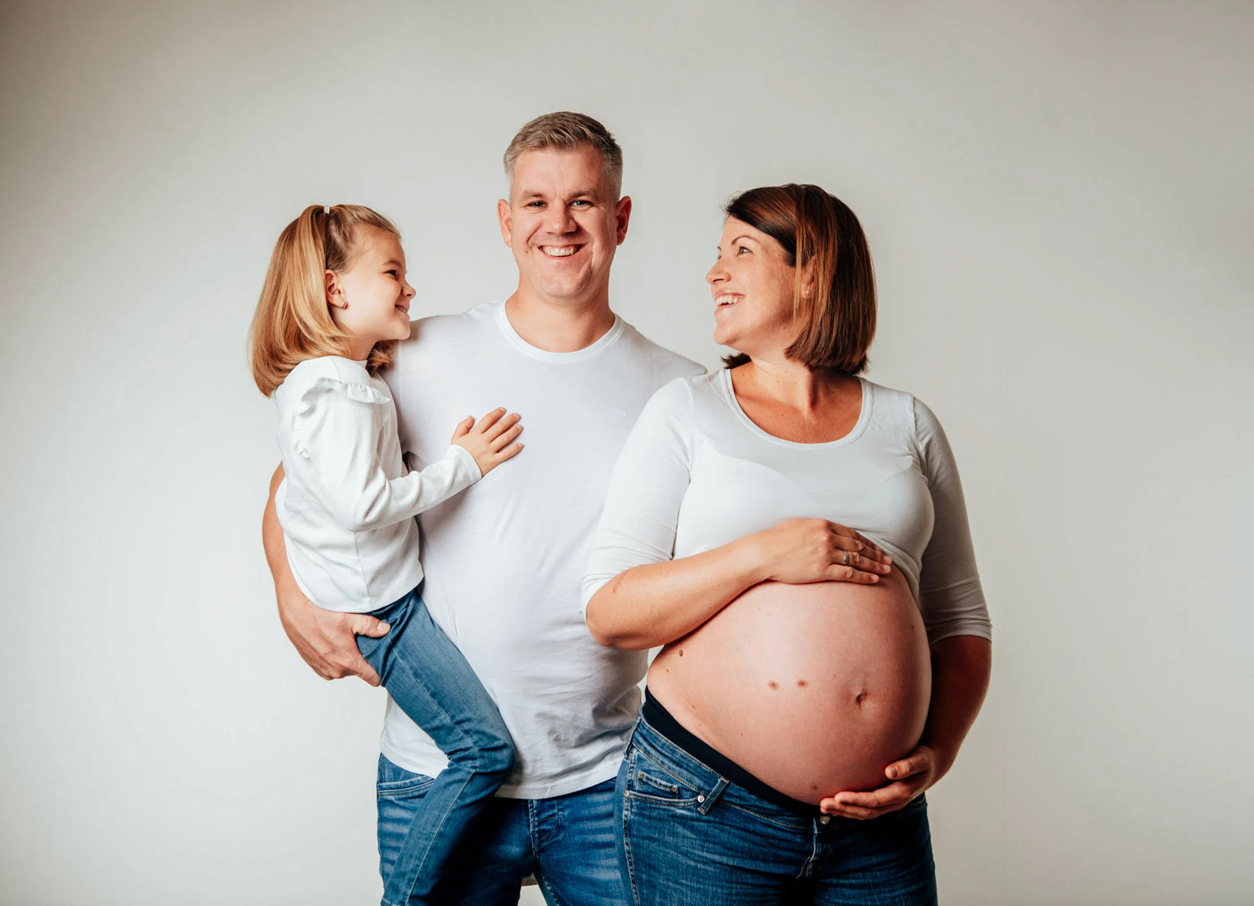 Shop: Babypass – Babybauch mit Familie | Peter Lauritis Photography Babybauch mit Familie: Papa trägt die Tochter, Mama zeigt lachend ihren Babybauch
