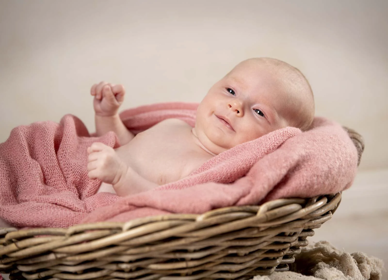 Babypass-Zusatztermin: lächelndes Baby mit erhobener Hand im rosa Tuch in einem Weidenkorb