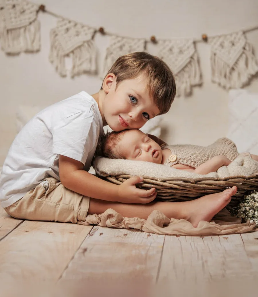 startseite babypass kombipaket Kachel | Peter Lauritis Photography Großer Bruder hält sein schlafendes neugeborenes Geschwisterchen im Korb – Babyfotos im Fotostudio