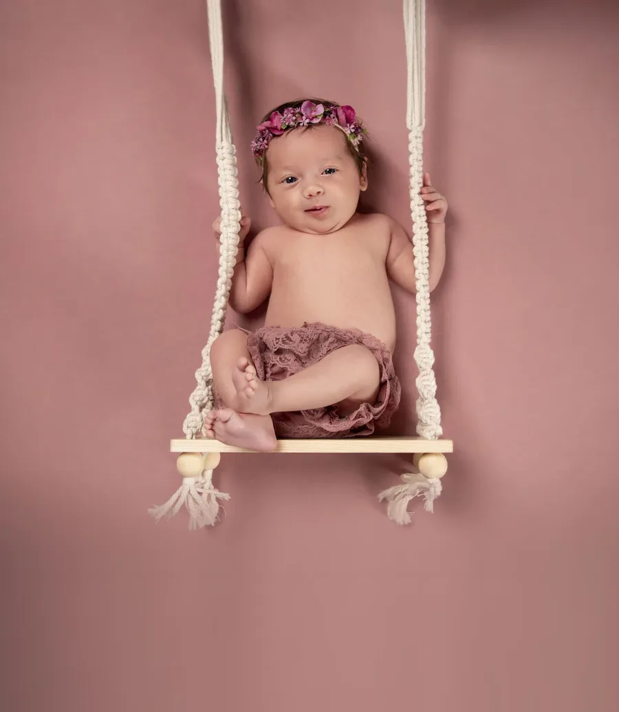 startseite neugeborene baby schaukel Kachel | Peter Lauritis Photography Lächelndes Baby mit Blumenhaarband in einer Makramee-Schaukel vor rosa Hintergrund – Babyfotos im Fotostudio
